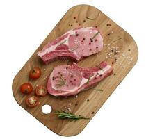 Raw pork tenderloin on the bone and spices on a wooden cutting board on a white isolated background. Portion for lunch and dinner, top view photo