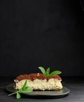 A piece of tiramisu sprinkled with cocoa, on top of a sprig of fresh mint on a black background photo