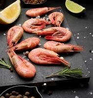 Boiled shrimp on a board, lemon slices, spices on a black background photo