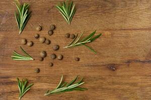 Dry allspice peas and rosemary branches on a wooden background photo