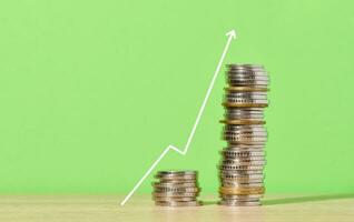 A stack of metallic coins and a graph on a green background. Income growth in business, high profitability photo