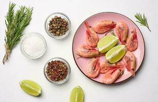 Boiled shrimp, lemon and lime slices, spices in a round pink plate on a white background top view photo