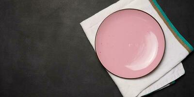 Empty pink ceramic plate on black table, top view photo