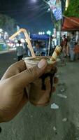 Street Chocolate Coffee Frappe Cup in Young Caucasian Hand natural blur Background. night shoot with lowlight capture. photo