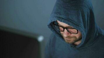 Male hacker in the hood and glasses working on a computer in a dark office room. Cybercrime concept video