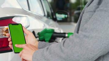 Woman uses a mobile application in a smartphone to pay for refuelling a car. Smartphone with a green screen. Chroma key video