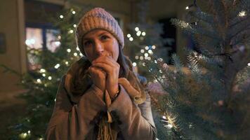 Porträt von ein glücklich Frau gegen das Hintergrund von Weihnachten Dekorationen. sie reibt ihr Hände, behalten Sie warm von das kalt. Weihnachten und Neu Jahr Ferien Konzept video