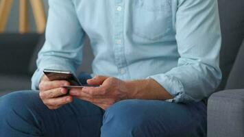 Formally dressed man sits on a sofa and enters a credit card number into a smartphone to pay online. Online shopping video