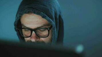 masculino hacker en el capucha y lentes trabajando en un computadora en un oscuro oficina habitación. cibercrimen concepto video