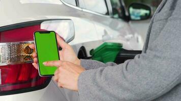 mujer usos un móvil solicitud en un teléfono inteligente a pagar para repostaje un coche. teléfono inteligente con un verde pantalla. croma llave video