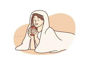 Girl with cup of hot coffee lies wrapped in blanket and smiles enjoying winter morning. Woman drinking hot drink with blanket to keep warm after walking on cold street for autumn mood concept vector