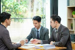 Asian business team consists of marketing staff. accountant and financial officer Help each other analyze company profits using graph paper, and corporate pens. photo