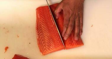 Chef Cutting The Salmon Meat Fillet In Half And Separating From Its Skin For Sushi Dish. - high angle shot video