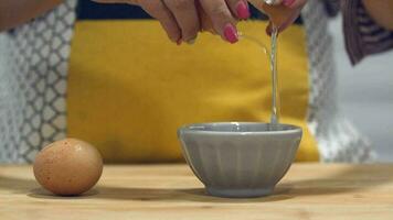 A married woman is cracking an egg in a ceramic bowl - medium shot video