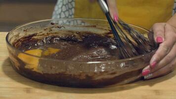 A woman mixing eggs in a chocolate batter kept in a transparent bowl - medium shot video