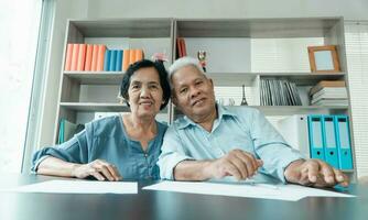 Senior Asian couple using the calculator and paperwork on desk at home to calculate expenses and income. And savings after retirement. Concept of financial planning and investment for retirees. photo