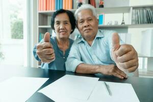 Senior Asian couple using the calculator and paperwork on desk at home to calculate expenses and income. And savings after retirement. Concept of financial planning and investment for retirees. photo