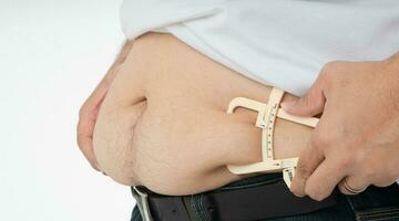 Close up of fat man hands measuring overweight belly by using body fat caliper photo