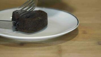 A person is cutting a heart-shaped cake using knife and fork on a white plate kept on the table - slow motion video