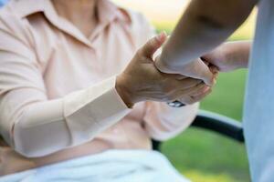 Happy senior Asian grandmother uses wheelchair with her daughter and grandchild in park, Grandson came to visit elderly grandmother and hold hand. Concept of happy family, good relationship together photo