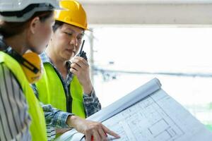 Asian engineer or Young Female Architect put on a helmet for safety and talk with a contractor on a construction building factory project, Concept of Teamwork, Leadership concept. photo