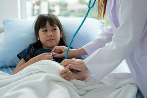 una médica pediatra asiática sostiene un estetoscopio para examinar a una niña paciente y los pulmones del corazón de un niño, un buen médico de familia que visita a un niño en casa, atención médica y medicina para el concepto de infancia. foto