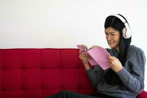 Cute Asian woman is sitting on the sofa in the morning And reading a book While listening to music In the living room photo