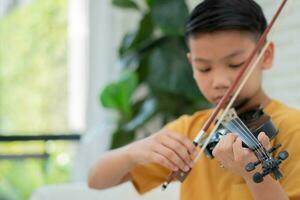 un pequeño asiático niño jugando y práctica violín musical cuerda instrumento en contra en hogar, concepto de musical educación, inspiración, adolescente Arte colegio alumno, selectivo enfocar. foto