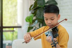 un pequeño niño asiático tocando y practicando violín instrumento de cuerda musical en casa, concepto de educación musical, inspiración, estudiante de escuela de arte adolescente. foto