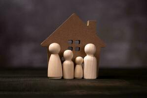 figuras de madera familia de pie frente a una casa de madera. el concepto de protección y seguridad, seguridad en el hogar, seguro de propiedad y casa. foto