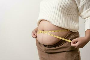 un obesidad utilizando medición cinta a espectáculo el real tamaño. gordito grasa mujer utilizando medida cinta a barriga. foto