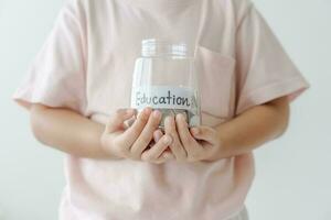 Kid holding her saving coins jar concept of savings money for future education school admission fee. Little daughter learn to save money. photo