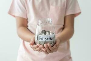 Kid holding her saving coins jar concept of savings money for future education school admission fee. Little daughter learn to save money. photo