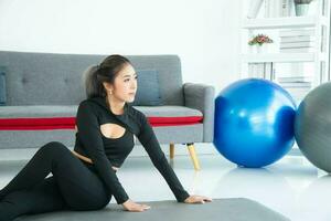 asiático joven sano mujer en material deportivo practicando yoga a hogar, deporte niña ejercicio en vivo habitación a hogar foto