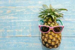 Pineapple with pink sunglasses on blue wooden background photo