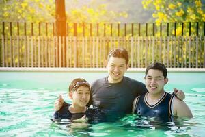 padre y sus dos hijos juegan en una piscina de agua clara - concepto de tiempo de juego familiar feliz foto