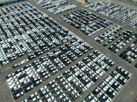 Aerial view of new cars stock at factory parking lot. Above view cars parked in a row. Automotive industry. Logistics business. Import or export new cars at warehouse. Big parking lot at port terminal photo
