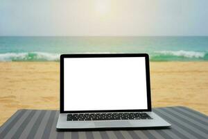 Laptop with blank screen for creative design on beach bed nearby beach and blue sea background. Computer notebook with clipping path for present landing page design mock up template photo