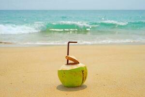 Selective focus of fresh coconut juice and straw on tropical sand beach nearby blue sea scene. Tropical fruit juice for healthy background. photo