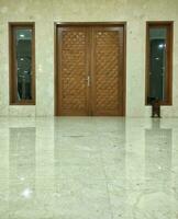 Bandung, Indonesia, 2023 - Brown closed wooden door with two windows in a creamy wall and marble floor in the Al Aziz Mosque, brown closed wooden door with copy space photo