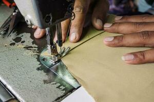 Close up view of sewing process. Hands stitching fabric on professional manufacturing machine at workplace photo