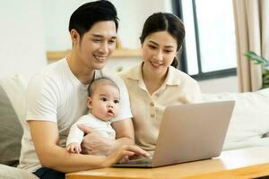 image of asian family with baby sitting on sofa using laptop photo