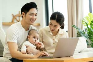 image of asian family with baby sitting on sofa using laptop photo