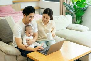 image of asian family with baby sitting on sofa using laptop photo