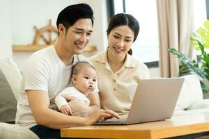 image of asian family with baby sitting on sofa using laptop photo