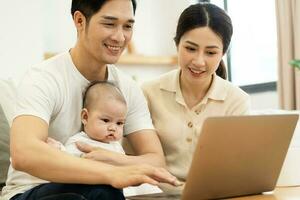 image of asian family with baby sitting on sofa using laptop photo