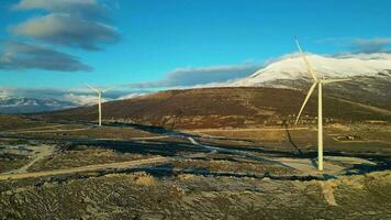 Windmühlen auf den Hügeln bei Sonnenuntergang. erneuerbare energie, grüne energie. Berge im Hintergrund mit Schnee. Windkraft und umweltfreundlich. nachhaltige Zukunft. Schluss mit fossilen Brennstoffen. video