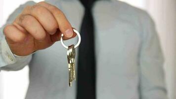 Mann im ein passen Stehen im Vorderseite von das Hintergrund zeigen das Schlüssel zu ein Neu Haus, das Bild von das Haus Schlüssel benutzt zum echt Nachlass Anzeigen video