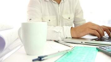 arquitecto mirando a proyectos a computadora y Bebiendo café a relajarse, hombre mecanografía con ordenador portátil sentado a escritorio, selectivo atención video