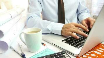 Corporate businessman working at office desk, architect typing with laptop, cup of coffee on foreground, selective focus video